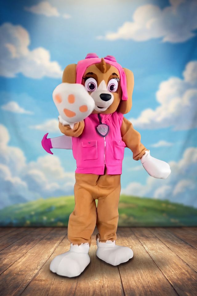 Stella en costume de mascotte, sur une scène de théâtre, devant un ciel bleu nuageux.