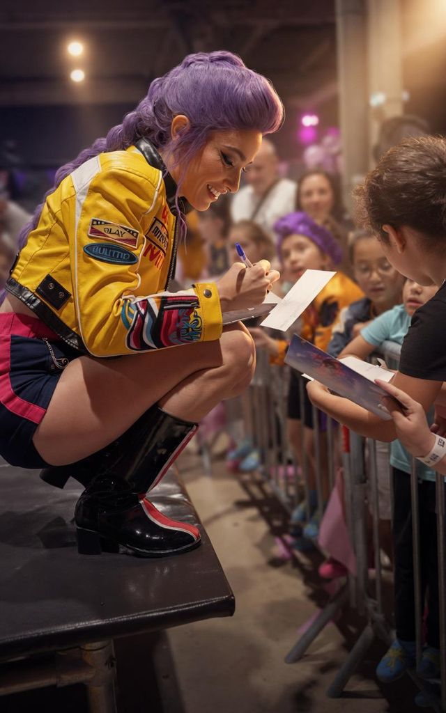 Une cosplayeuse en veste jaune signe des autographes à des enfants derrière une barrière.